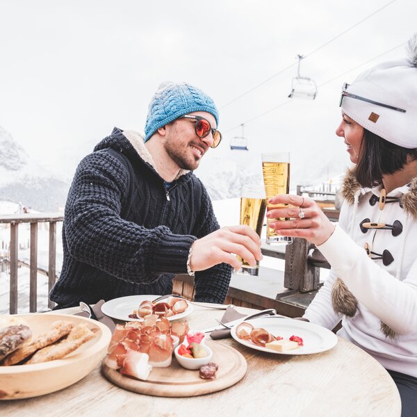 Coppia fa un brindisi durante un aperitivo in rifugio ad alta quota in inverno | © Patricia Ramirez  - Archivio Immagini ApT Val di Fassa